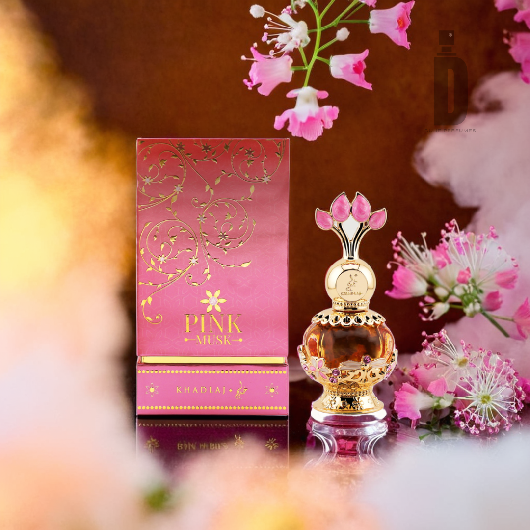 A luxurious bottle of Pink Musk 20ml Perfume Oil by Khadlaj, featuring a pink and gold decorative design, is elegantly displayed next to its matching box. Soft pink blossoms and gentle white clouds of mist envelop the arrangement, with a subtle hint of fragrance oil on a warm, brown background.