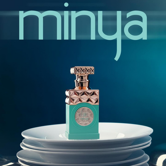 A decorative perfume bottle from Paris Corner, labeled as "Minya 100ml EDP," is elegantly positioned on a stack of white plates against a blue background. The rectangular bottle boasts a teal base adorned with gold geometric patterns, radiating luxury. The word "minya" stands out boldly, suggesting the alluring salted caramel fragrance housed within its 100ml capacity.