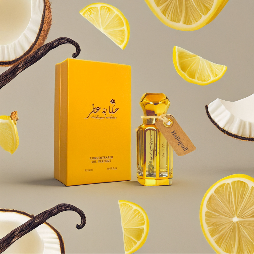 A yellow "Hallopuff 12ml Perfume Oil - Hekayat Attar" bottle and box are beautifully displayed among vanilla bourbon pods, lemon slices, and coconut cream pieces on a neutral background. A "Halal" tag hangs from the gourmand-floral fruity scent-filled bottle by Hekayat Attar.