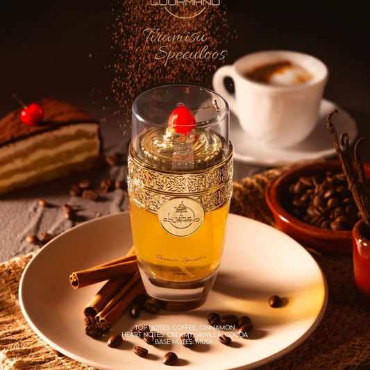 A luxurious bottle of Tiramisu Speculoos 100ml EDP by Paris Corner, embellished with intricate gold detailing and topped with a cherry, rests on a plate surrounded by coffee beans and cinnamon sticks, releasing a rich dessert aroma. In the background, a slice of Tiramisu Speculoos accompanied by a cup of coffee enhances the indulgent sensory experience.