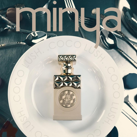 On a white plate inscribed with "COCO LUSH," a perfume bottle featuring a studded cap is elegantly placed. Surrounding it are scattered spoons and a knife, creating an aura of mystery. The name "Minya Coco Lush 100ml EDP" from Paris Corner subtly appears above, hinting at the enchanting jasmine notes wafting through the air.