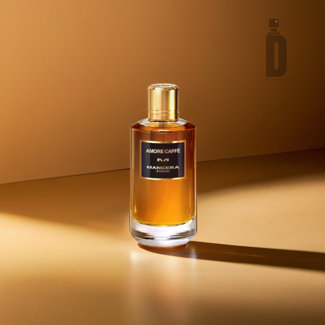 A clear, upright bottle of Amore Caffe 120ml EDP by Mancera, featuring a golden cap, is set against a warm, golden backdrop. The bottle contains a rich amaretto and amber-hued liquid that gently reflects the light.