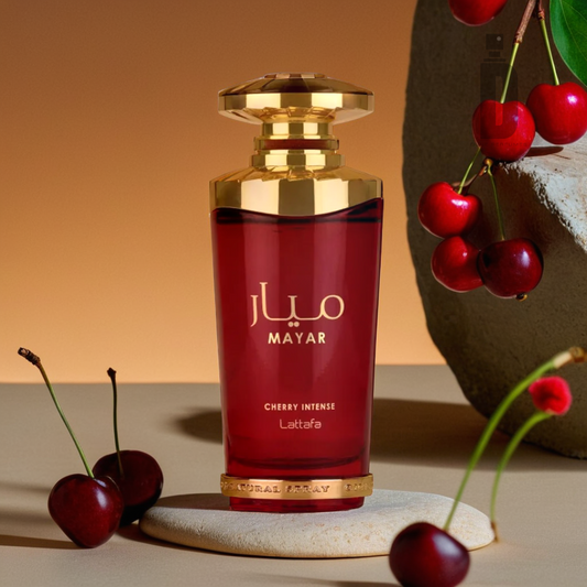 A luxurious red and gold perfume bottle labeled "Mayar Cherry Intense 100ml EDP - Lattafa" sits on a table, showcasing the "Lattafa" branding. Cherries, reminiscent of the Cherry Intense fragrance's essence, are scattered around, with some hanging from a branch against a backdrop of warm brown and orange gradients.