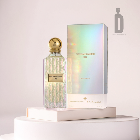 A luxurious Cullinan Diamond Iris 200ml EDP bottle from Ibrahim Al Qurashi, featuring a diamond pattern and gold cap, is elegantly paired with its iridescent box. Both sit on a white circular platform, radiating opulence against the minimalist backdrop.