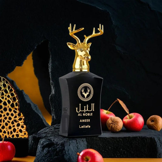 A black perfume bottle labeled "Al Noble Ameer 100ml EDP - Lattafa" from Lattafa sits on a dark background with a gold deer head as its cap. Surrounding the bottle are small red apples, walnuts, and a gold decorative object, creating an elegant display that hints at notes of oud and patchouli.