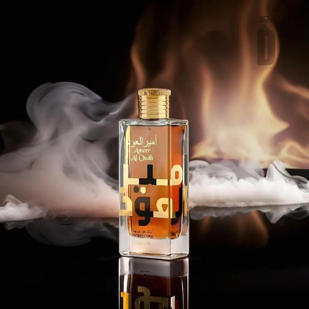 A clear glass perfume bottle labeled "Ameer Al Oud Intense 100ml EDP - Lattafa" stands on a reflective black surface with swirling smoke and a warm, golden background. The bottle features amber-colored liquid and a golden cap. Arabic text, hinting at the rich notes of agarwood, is visible on the label.