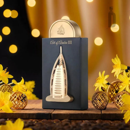 A 100ml bottle of Art of Arabia III Eau de Parfum by Lattafa, featuring an elegant gold cap and a design reminiscent of a skyscraper, stands on a wooden surface. Partially encased in a black box labeled "Art of Arabia III," the scene is complemented by yellow flowers and decorative gold spheres, evoking an exotic allure fitting for this Arabian fragrance.