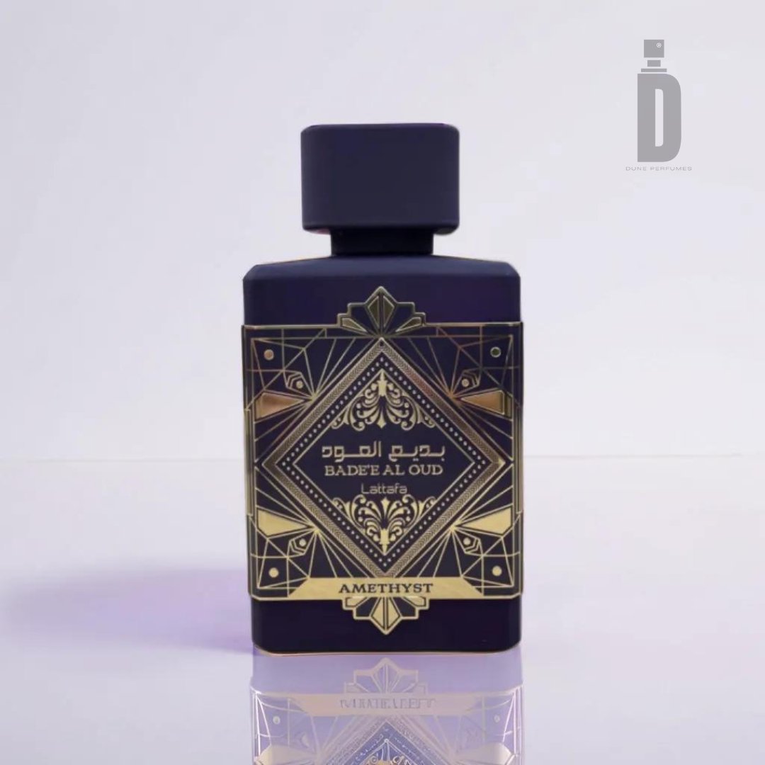 A perfume bottle labeled "Badee Al Oud Amethyst 100ml EDP" by Lattafa, featuring an intricate gold and black geometric design with "Amethyst Fragrance" written at the bottom. The rectangular-shaped bottle is adorned with a rounded black cap and placed against a plain background, exuding the essence of agarwood (oud) and Turkish rose.