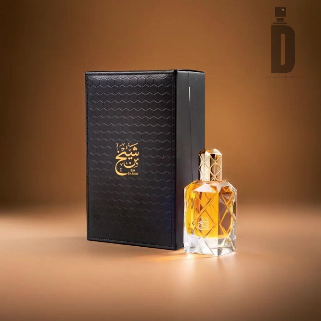 A luxurious scent set, "Bin Shaikh 90ml EDP - Ahmed Al Maghribi," features a hexagon-patterned black box with gold Arabic script next to a geometric glass perfume bottle filled with amber liquid. The background is a gradient of warm tones. A logo with "I D Dubai Perfumes" is visible in the top right corner, exuding Arabic grandeur.