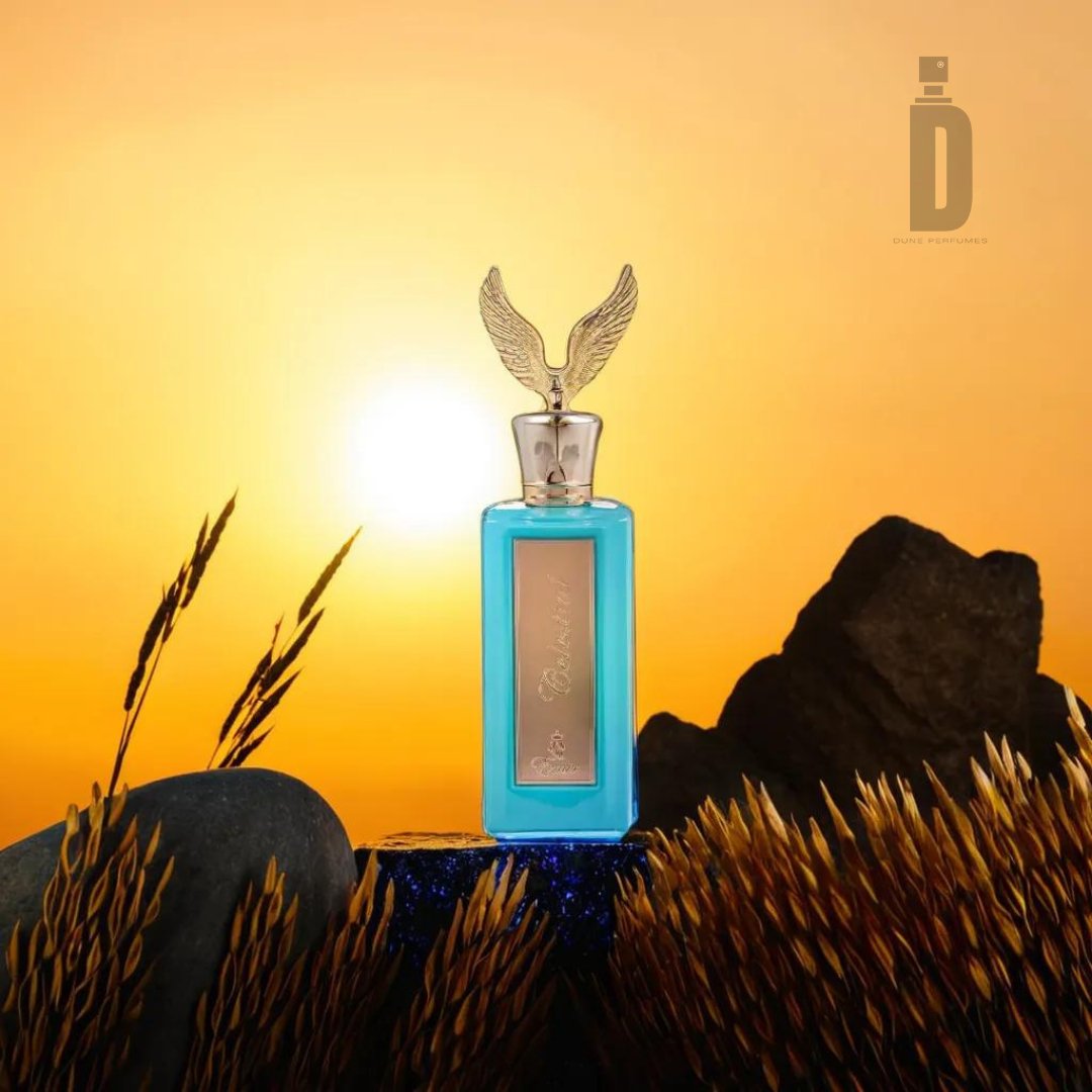 A turquoise perfume bottle with a winged gold cap stands among rocks and wheat stalks, with a vibrant sunset in the background. The logo of "Paris Corner" appears in the top right corner, hinting at an ethereal blend within this Celestial 100ml EDP - Emir fragrance.