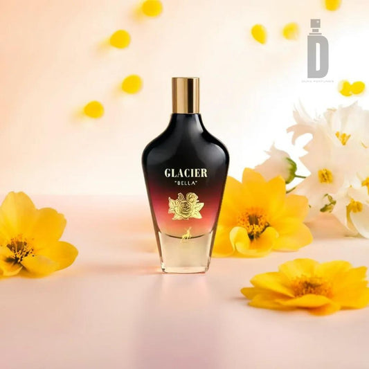 A fragrance bottle labeled "Glacier Bella 100ml EDP - Maison Alhambra" is positioned in the center, flanked by yellow flowers and white daffodils. This captivating fragrance, from Maison Al Hambra, features a gradient design transitioning from dark to light, topped with a gold cap. The background is softly lit and decorated with petals.