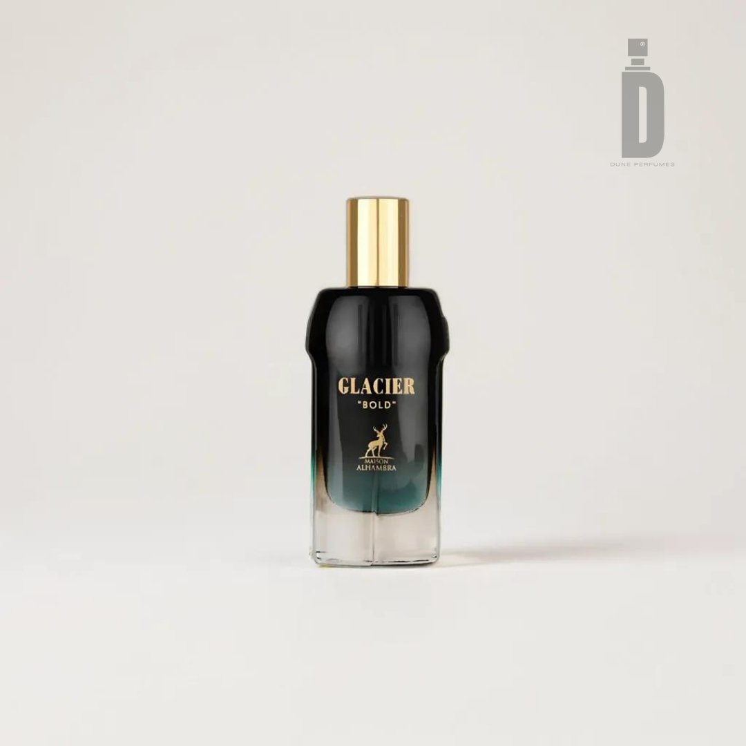 A bottle of Glacier Bold 100ml EDP by Maison Alhambra stands against a plain white background. The rectangular bottle with curved edges features a black and gold gradient design. The cap is gold, and the minimalist label, adorned with a leaping deer logo and text, “GLACIER BOLD,” hints at notes of bergamot and tonka bean.