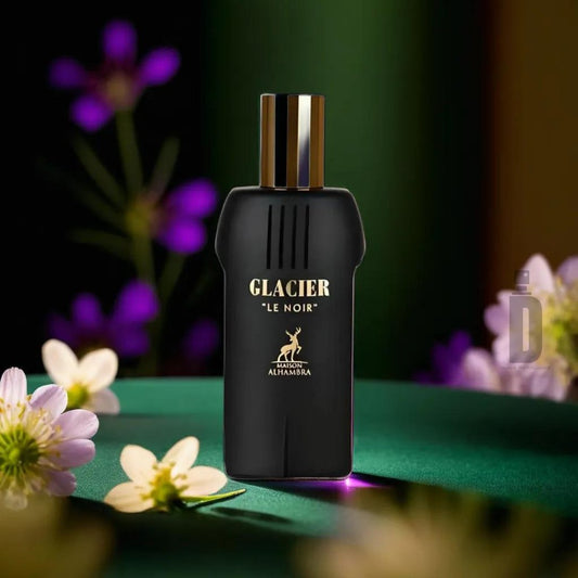 A bottle of Glacier Le Noir 100ml EDP from Maison Alhambra is centered on a green surface adorned with white and purple flowers. The sleek black design, complemented by a metallic gold cap, exudes sophisticated allure. The brand name "Maison Al Hambra" and the fragrance name "Glacier Le Noir 100ml EDP" are elegantly displayed in white against a dark, softly lit background.