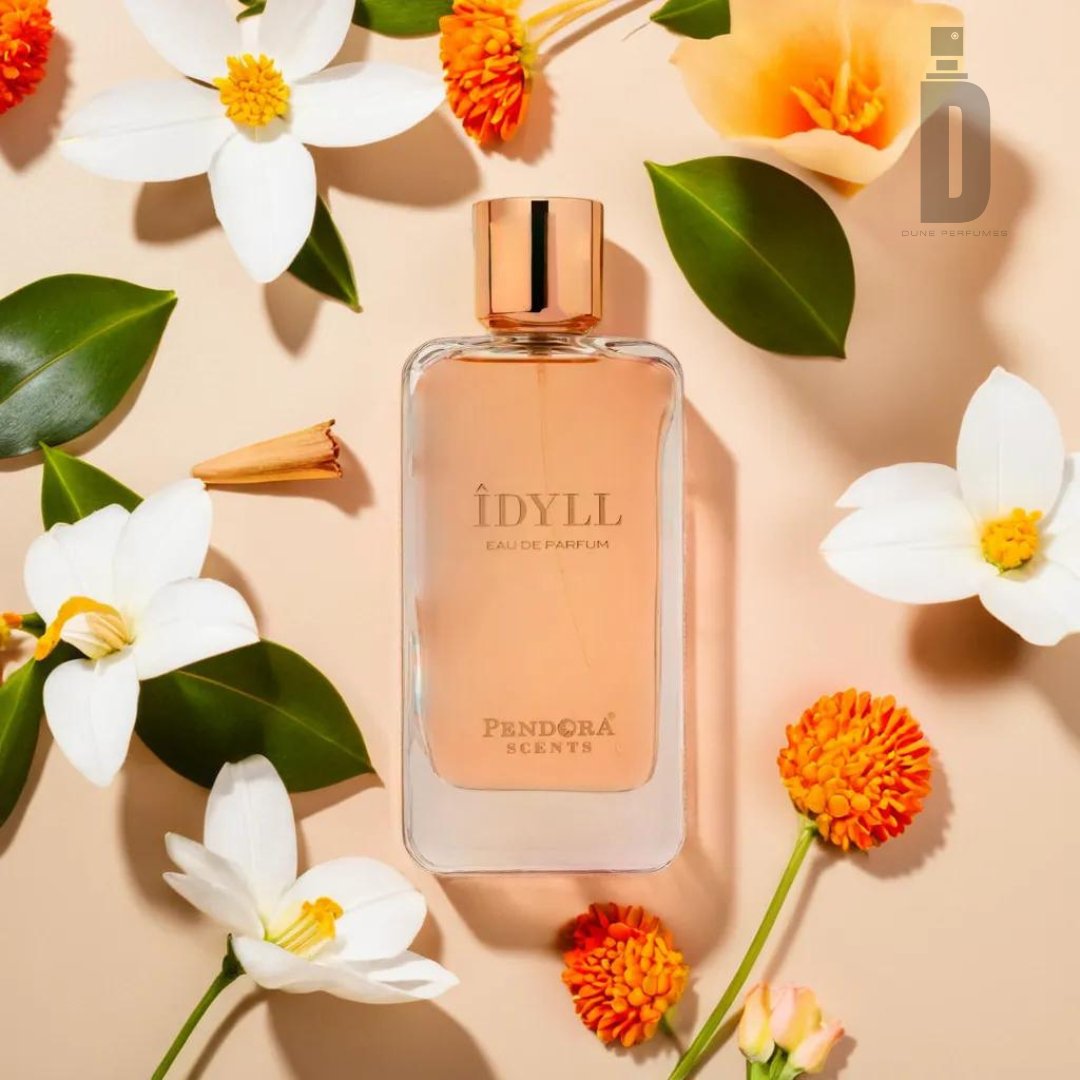 A bottle of Idyll 100ml EDP by Paris Corner is placed amidst white and orange flowers and green leaves on a beige background. The bottle, with a gold cap and minimalist design, exudes a sophisticated scent. "Idyll" and "Paris Corner" are elegantly printed in gold on the bottle.