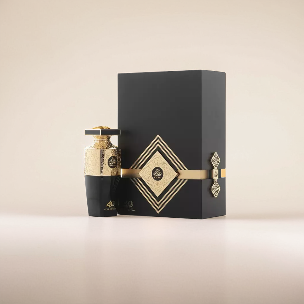 The Madawi Gold Edition 100ml EDP by Arabian Oud features a luxuriously black bottle with intricate gold patterns, capped in gold. It accompanies an elegant black-and-gold box with geometric designs and an ornate clasp, exuding a rich vanilla patchouli fragrance.