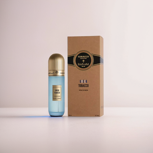 A blue cylindrical bottle labeled "Greek Tobacco 100ml EDP - Ibrahim Al Qurashi," with a gold cap, sits beside a matching brown box. The box, adorned with black and gold designs, reads "Tobacco Musk." Both items from Ibrahim Al Qurashi exude sophistication on a neutral-colored surface.