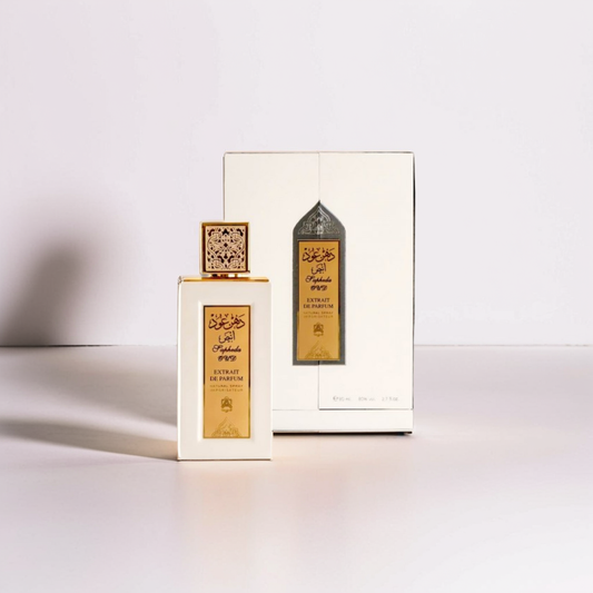 An 80ml Sapheda White Oud Extrait from Abdul Samad Al Qurashi stands before its ornate, gold and brown box adorned with Arabic script. The scent of Jasmine gently lingers as soft light casts a delicate shadow on the display.