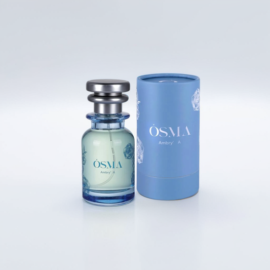 A blue glass bottle of Ambry A 75ml EDP by Osma stands beside its matching cylindrical box against a minimalistic gray background. A sleek silver cap crowns the light green liquid, exuding an elegant fragrance with subtle leather notes, both featuring identical branding.