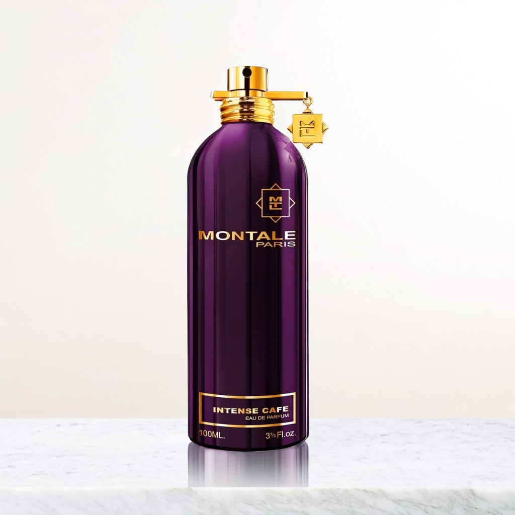 A tall, purple bottle labeled "Intense Cafe 100ml EDP - Montale" from Montale exudes an enchanting rose coffee fragrance. It features gold accents, a matching cap, and a hanging tag, standing elegantly on a marble surface against a light background.