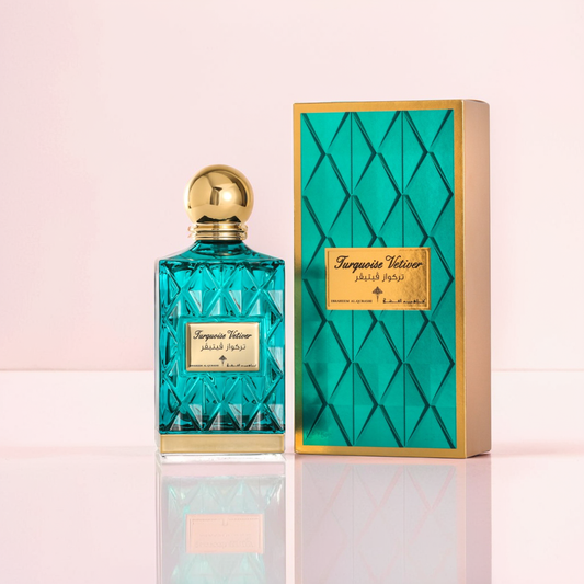 The Turquoise Vetiver 75ml EDP by Ibrahim Al Qurashi, featuring a turquoise bottle with a gold cap, stands beside its matching box adorned with a geometric pattern and gold label. The reflective surface below heightens the elegance of this captivating Ibrahim Al Qurashi fragrance.