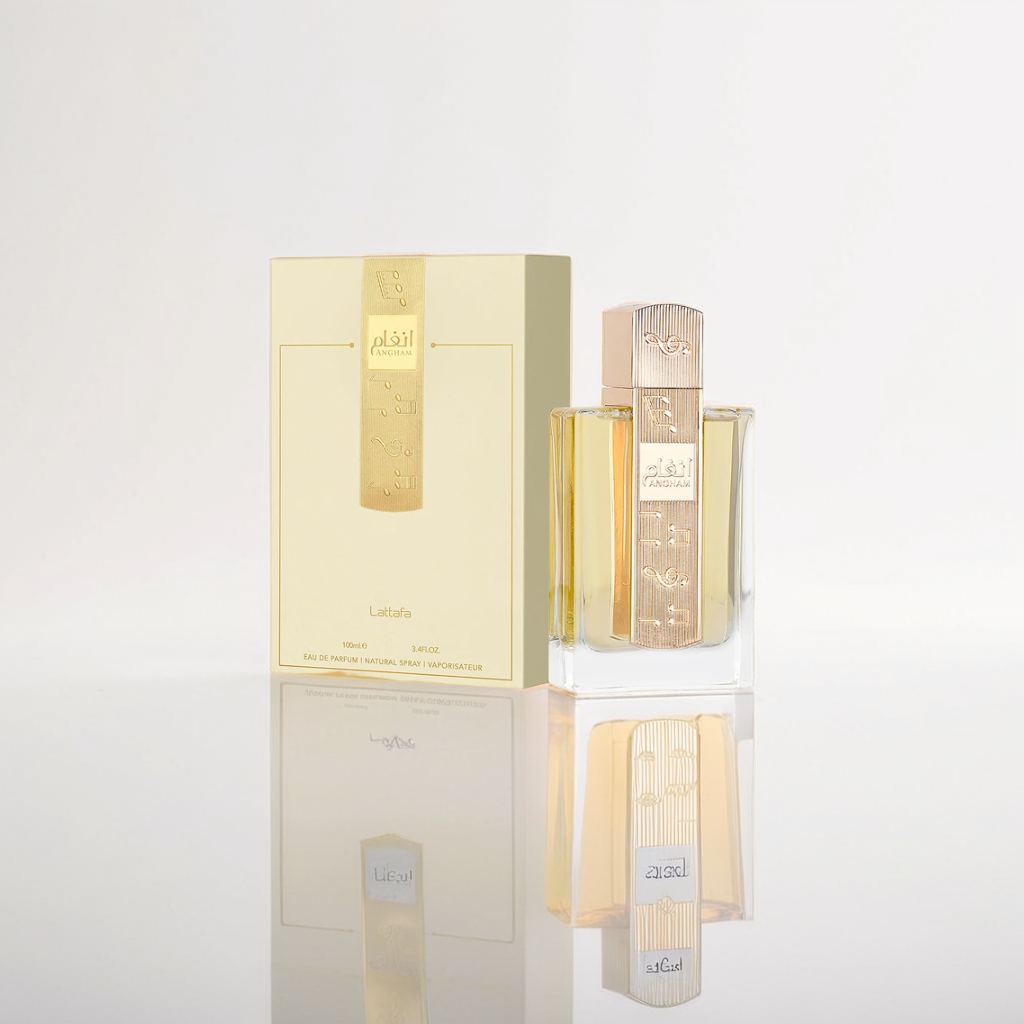 An Angham 100ml EDP by Lattafa, with a clear glass bottle and golden Arabic-scripted cap, sits beside a matching rectangular box on a reflective surface. The plain light-colored background highlights the mesmerizing essence of this Lattafa fragrance.