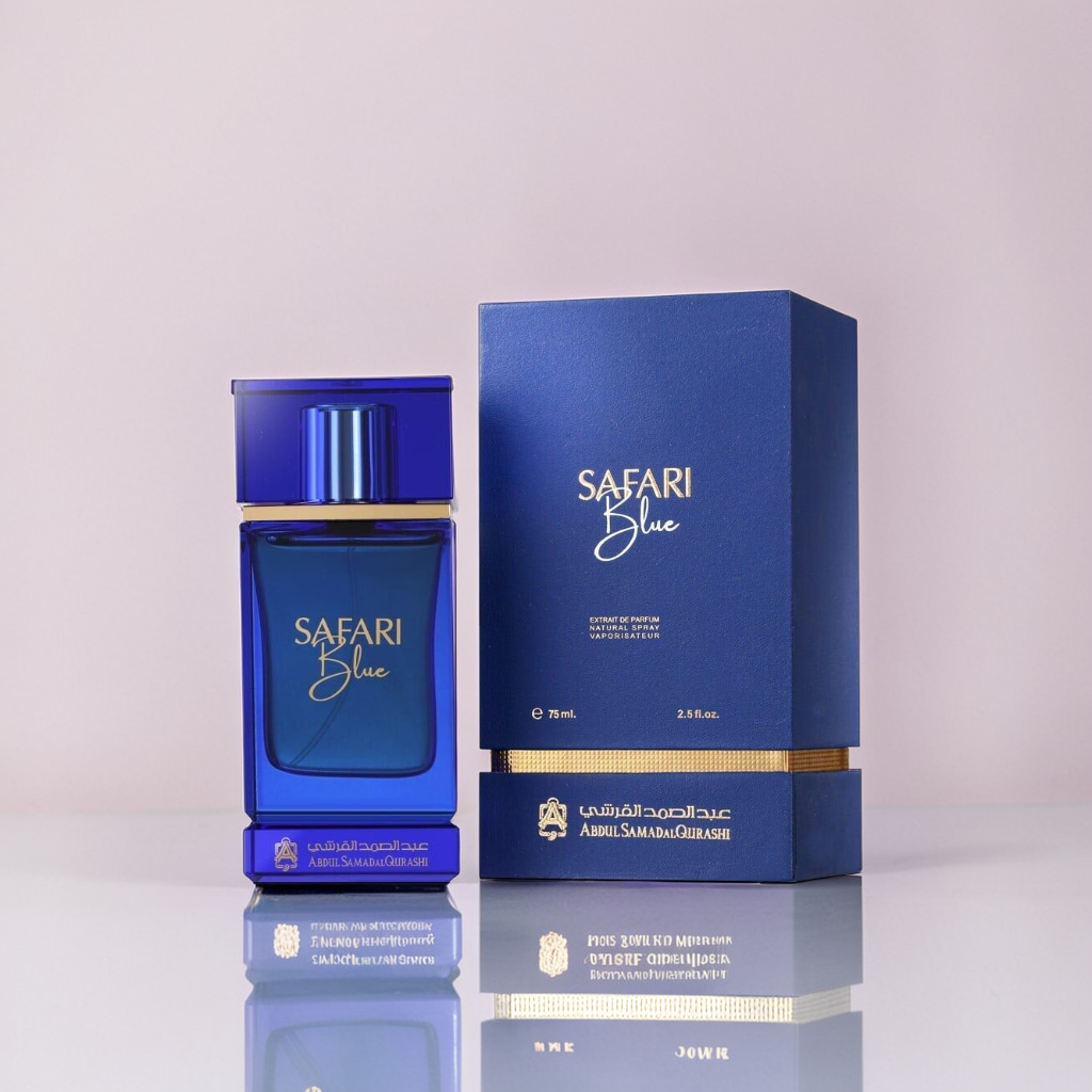 A blue glass perfume bottle labeled "Safari Blue 75ml EDP - Abdul Samad Al Qurashi" is paired with its matching rectangular box against a light pink background. Featuring Arabic and English text with white and gold accents, it promises an earthy undertone with citrusy and spicy notes.