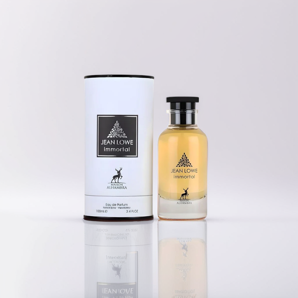 A 100ml bottle of Maison Alhambra's Jean Lowe Immortal EDP lies beside its matching cylindrical box, exuding timeless elegance. The light amber liquid, with a black cap and minimalist deer logo, embodies the bold fragrance within.