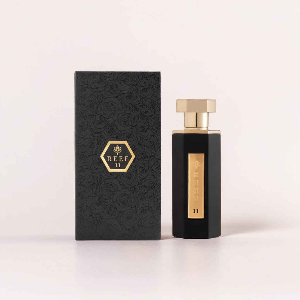 The 100ml EDP "Reef (11)" by Reef comes in a tall, black rectangular bottle with a gold cap, suggesting exotic ingredients. Its matching box features a floral pattern and a gold hexagonal logo, hinting at notes of jasmine and sandalwood.