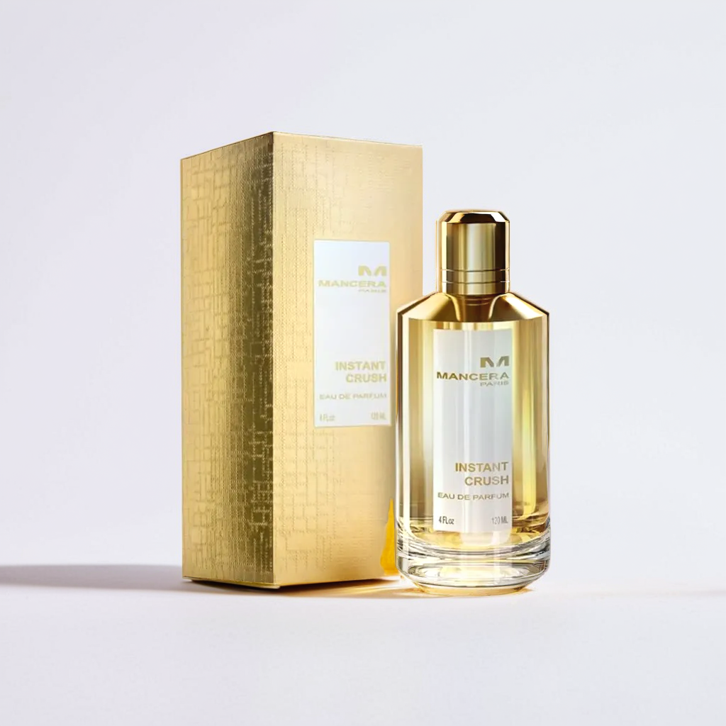 A bottle of Mancera's Instant Crush 120ml EDP, in a captivating gold finish, sits alongside its matching textured gold box on a white background. The bottle's shiny, reflective surface suggests the bold fragrance contained inside.