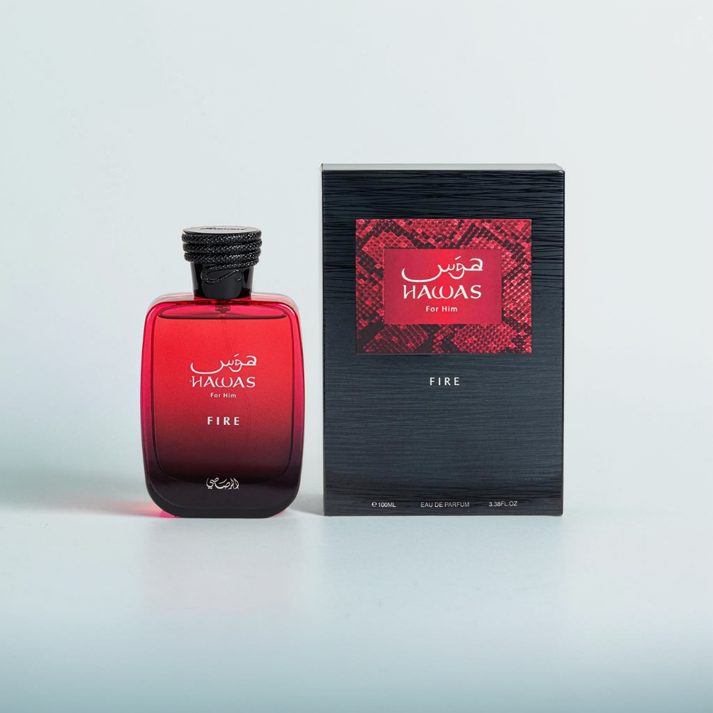 A 100ml red glass perfume bottle labeled "Hawas Fire" by Rasasi sits next to its matching black and red box. Accented with Egyptian jasmine and clary sage, the bottle features a black cap, while the box displays decorative patterns with Arabic and English text.