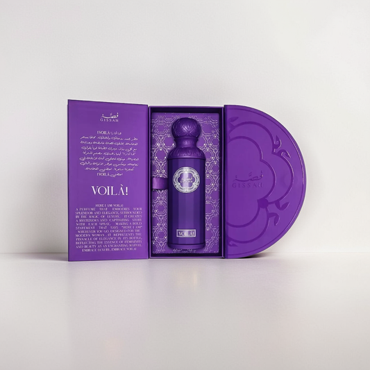 A purple cylindrical bottle of Gissah's Voila 200ml EDP with an ornate cap is placed in an elegant open purple box with a round lid. The box showcases intricate multi-language text and designs on a white background, suggesting the floral fragrance and subtle musk notes inside.