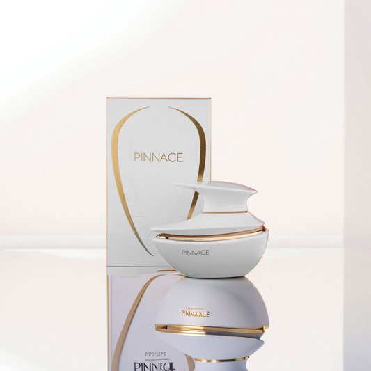 A sleek white Pinnace White 100ml EDP by Fragrance World, adorned with gold accents, elegantly sits in front of its matching box. This citrus-bright fragrance is perfectly reflected on the glossy surface, while a softly lit white backdrop enhances its allure.