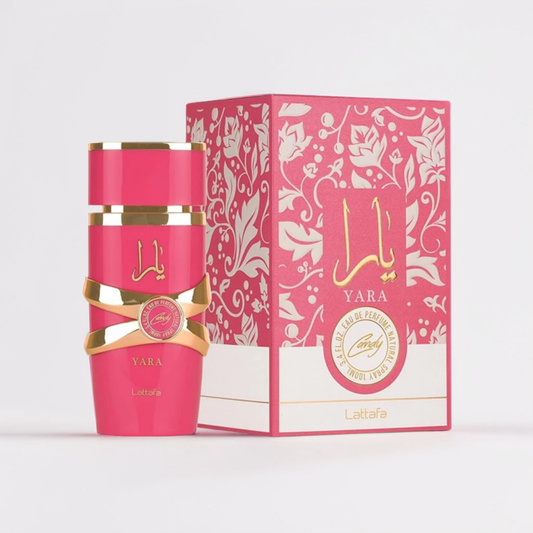 A pink "Yara Candy 100ml EDP" by Lattafa, adorned with gold accents, sits beside its matching box. Both display intricate floral designs that suggest a sweet blend of vanilla syrup and strawberry fizz candy. They elegantly rest on a plain white background.