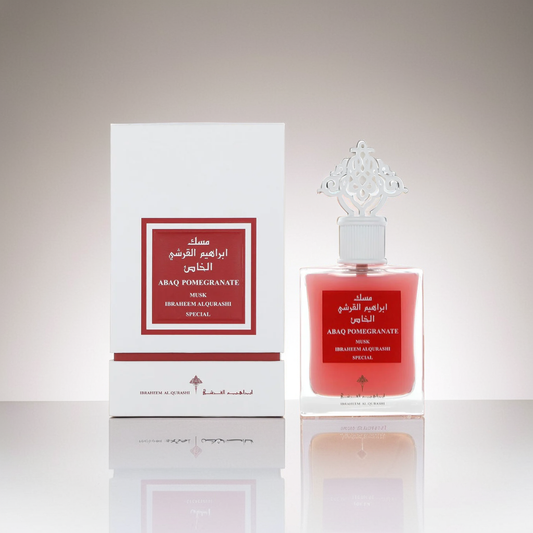 A 75ml EDP bottle labeled "Pomegranate Musk" from Ibrahim Al Qurashi, with an ornate silver cap, stands beside a matching rectangular box adorned with Arabic text. Placed on a reflective surface, it exudes a rich musk essence intertwined with hints of pomegranate.