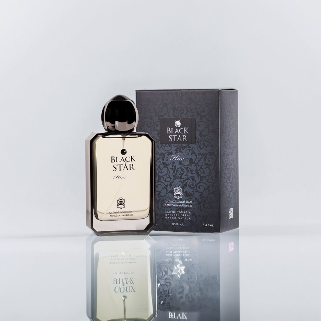 A 100ml bottle of Black Star Him EDP by Abdul Samad Al Qurashi stands elegantly beside its matching box. The clear bottle with a black cap displays the "Black Star Men" label, while the dark box with silver text mirrors woody elements, both beautifully reflected on the surface.