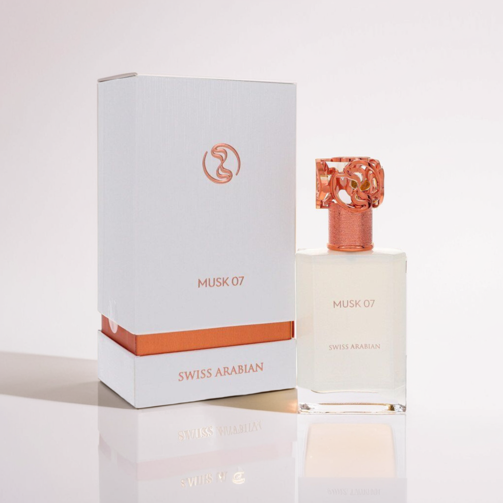 A 50ml Musk 07 Extrait bottle by Swiss Arabian stands beside its box, radiating musk notes. The bottle has a detailed orange cap and minimalist style, while the white packaging with orange details mirrors the fragrance's sophistication.