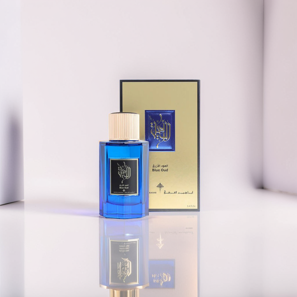 The Blue Oud 100ml EDP by Ibrahim Al Qurashi features a blue perfume bottle with a gold cap and Arabic script. It stands before a matching box with gold and blue design, also displaying the text "Blue Oud." Soft lighting adds an elegant touch reminiscent of fragrant Blue Lilies.