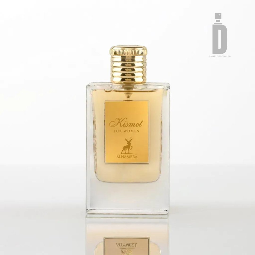 The product is a rectangular glass perfume bottle featuring a gold cap and label. The label displays the text "Kismet Women, Maison Alhambra" along with an illustration of a small animal below. The bottle holds 100ml of light yellow liquid, and the top right corner of the label showcases a logo that promises an enchanting aroma within.