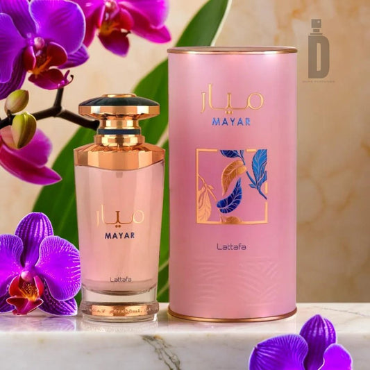 A bottle of Mayar 100ml EDP by Lattafa is beautifully displayed next to its cylindrical pink packaging. The bottle, embodying femininity with a golden cap and elegant design, stands out magnificently. Vibrant purple orchids in the background add a touch of color and natural beauty to the fragrant scene.