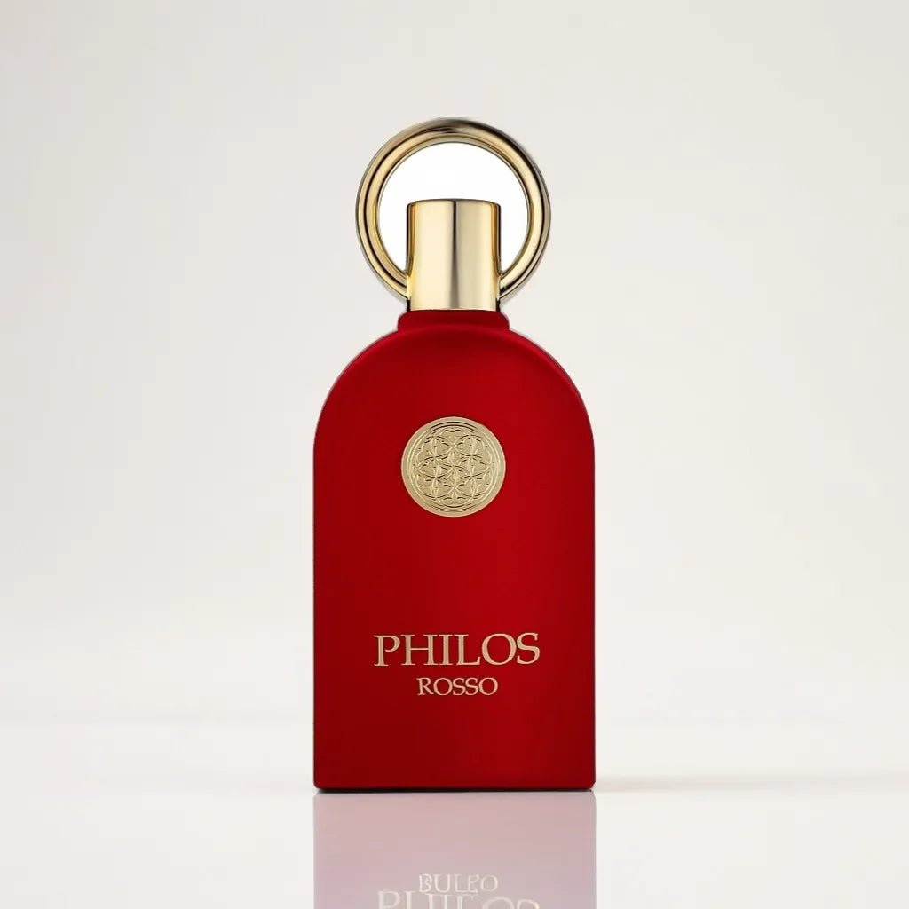 A luxurious red bottle of Philos Rosso 100ml EDP - Maison Alhambra stands against a white background, exuding refined elegance. The bottle features a gold circular emblem and a matching gold cap with an elegant, round handle on top. The "PHILOS ROSSO" branding is prominently displayed in gold letters.