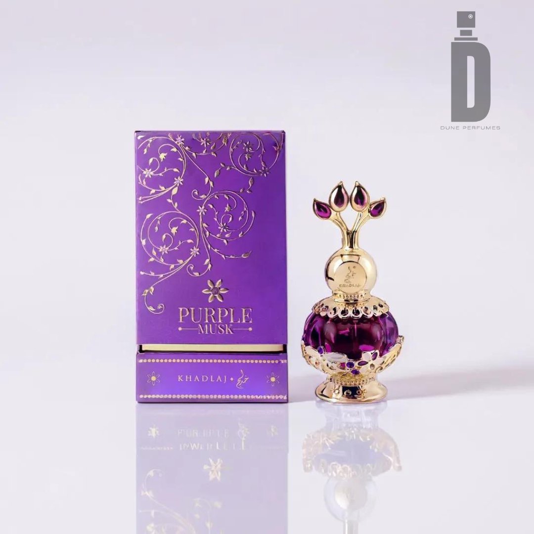 A decorative, ornate perfume bottle filled with purple-colored Purple Musk 20ml Perfume Oil - Khadlaj stands beside a purple and gold packaging box. The box is labeled "KHADLAJ PURPLE MUSK," featuring intricate gold floral designs. The bottle has an elaborate gold cap adorned with gem-like accents and a subtle Fruity Accord.