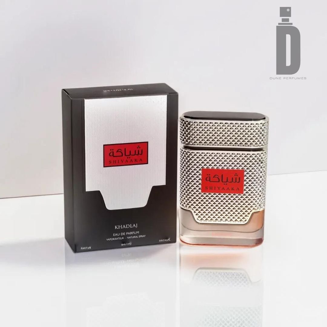 A perfume bottle of Shiyaaka For Men 100ml Eau de Parfum by Khadlaj and its accompanying box are placed on a white surface. The Eau de Parfum bottle has a metallic, textured design with red and black accents, showcasing Arabic text. The black box with white text and red and black accents mirrors the style of the bottle.