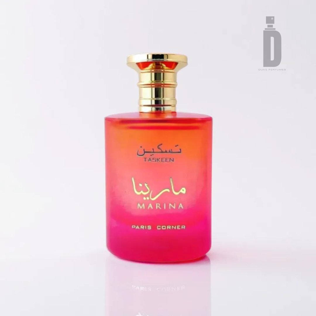 The Taskeen Marina 100ml EDP by Paris Corner showcases a beautiful gradient-toned bottle, transitioning from pink at the bottom to orange at the top, evoking images of tropical shores. Its elegant design is completed with a gold cap and text in both Arabic and English reading "Taskeen Marina" and "Paris Corner." The background is plain white with a faint shadow beneath the bottle.