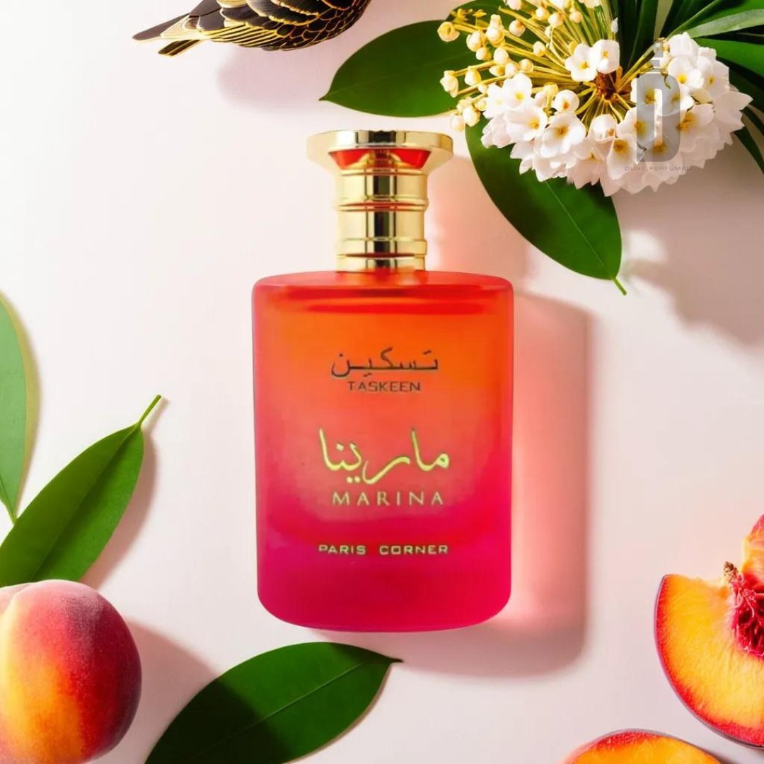 A pink and orange gradient perfume bottle labeled "Taskeen Marina 100ml EDP - Paris Corner" is surrounded by leaves, white flowers, a cut peach, and a bird at the top left. The bottle features a gold cap, evoking the light and airy feel of ocean breezes with natural elements.