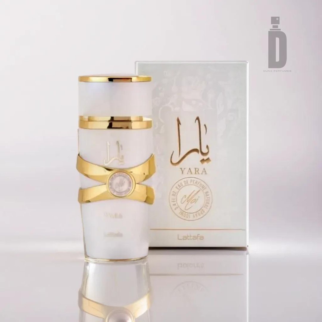 A frosted white cylindrical perfume bottle with gold accents, labeled "Yara Moi" in both Arabic and English, is placed in front of a matching box featuring the same labeling. This 100ml Eau De Parfum by Lattafa promises an unforgettable fragrance experience.