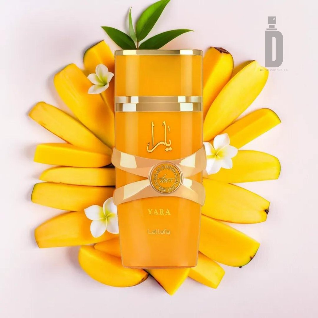 A vibrant orange bottle of "Yara Tous 100ml EDP - Lattafa" perfume stands elegantly amidst neatly arranged mango slices and white flowers. The exotic fragrance is highlighted with gold accents and a silver emblem, topped by a green leaf, while the logo in the top right corner encapsulates its tropical allure.